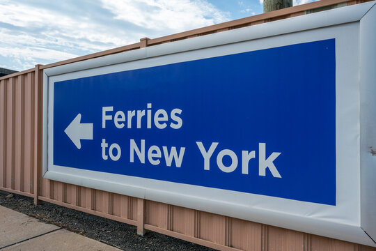 Directional Sign Pointing Towards Ferries to New York Under Cloudy Skies
