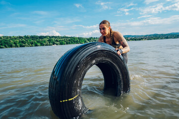 Muscular woman pushing tractor tire out of the water during an OCR race