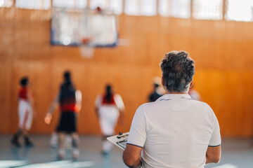 Rear view of a professional basketball coach watching training on court.