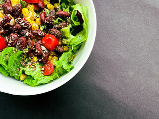 Healthy Green  lettuce salad with cherry tomatoes, corn, beans and seeds on dark background
