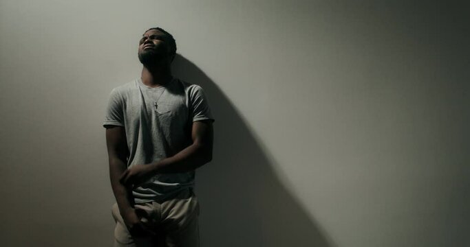 A bearded man in casual clothes leaned his head against the wall with a depressed look. Dim indoor lighting