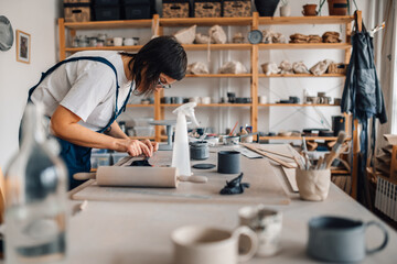 A potter is making earthenware and modeling wet clay at pottery workshop.