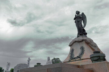 Sword-bearing angel and other statues peeking over graves on Avenida Cristobal Colon Avenue west side, Cementerio de Colon Cemetery. Havana-Cuba-094