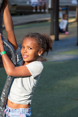 A smiling African American girl with curly hair climbs on playground equipment, capturing active...