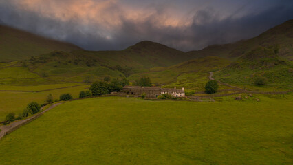 Fototapeta na wymiar AERIAL: Traditional old farmhouse located in green countryside of Lake District