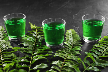 Absinthe in shot glasses and green leaves on black table, closeup. Alcoholic drink