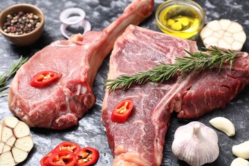Fresh raw beef cuts and different spices on grey textured table, closeup