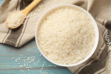 Raw basmati rice in bowl and spoon on light blue wooden table, top view