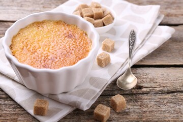 Delicious creme brulee in bowl, sugar cubes and spoon on wooden table, closeup