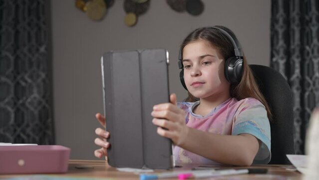 Happy girl with headphones looking to tablet camera, smiling, making faces using app with masks. Child having fun, listen to music, playing, having video call. Communication online distantly