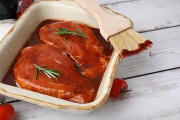 Raw marinated meat, rosemary and basting brush on white wooden table, closeup