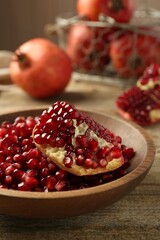 Ripe juicy pomegranate grains in bowl on wooden table, closeup