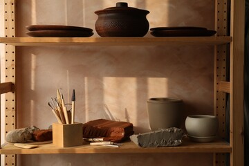Set of different crafting tools and clay dishes on wooden rack in workshop