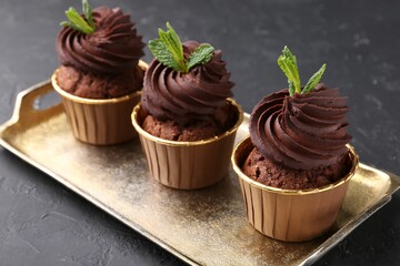 Delicious chocolate cupcakes with mint on black textured table, closeup