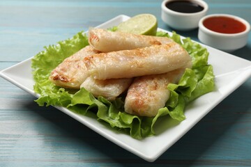 Delicious fried spring rolls served on light blue wooden table, closeup