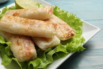 Delicious fried spring rolls on light blue wooden table, closeup