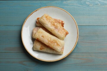 Delicious fried spring rolls on light blue wooden table, top view