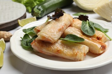 Plate with tasty fried spring rolls and spinach on white tiled table, closeup