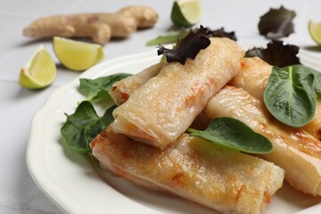 Plate with tasty fried spring rolls and spinach on white table, closeup