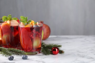 Aromatic Sangria drink in glasses, ingredients and Christmas decor on white marble table, space for text