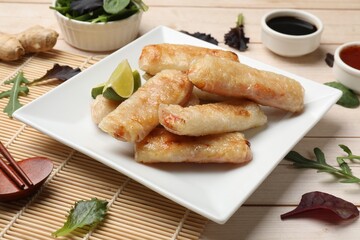 Tasty fried spring rolls, lime, sauces and other products on light wooden table, closeup