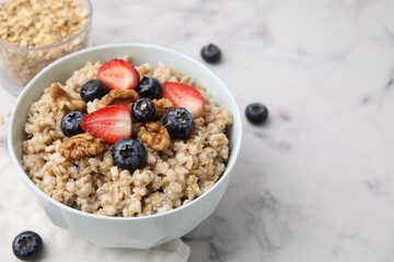 Tasty oatmeal with strawberries, blueberries and walnuts in bowl on white marble table. Space for text