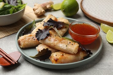 Tasty fried spring rolls, lettuce and sauce on grey table, closeup
