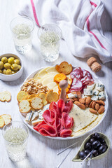 Aperitif, champagne and snack of sausage, cheese, nuts, olives and crackers on a light background. - 764309956