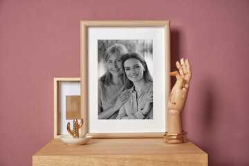 Black and white family portrait of mother and daughter in photo frame on table near color wall