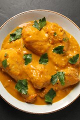 Tasty chicken curry with parsley on black textured table, top view