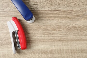 Color staplers on wooden table, flat lay. Space for text