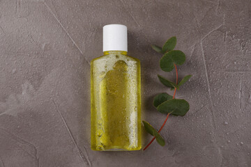 Fresh mouthwash in bottle and eucalyptus branch on dark textured table with water drops, top view