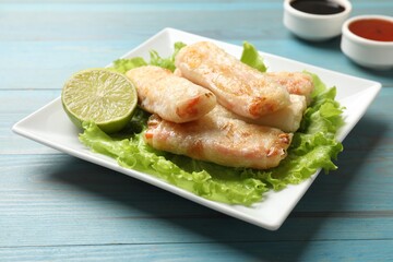 Delicious fried spring rolls on light blue wooden table