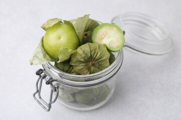 Fresh green tomatillos with husk in glass jar on light table, closeup
