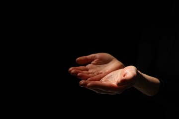 Religion. Woman with open palms praying on black background, closeup. Space for text