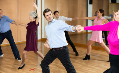 Positive adult man enjoying active dances with female partner in modern dance studio, practicing playful jitterbug moves