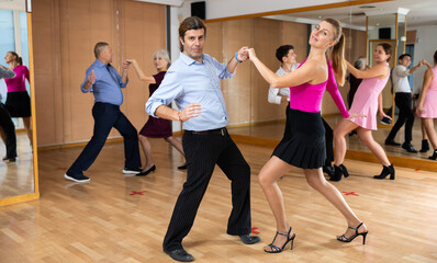 Fototapeta na wymiar Positive man and woman dancing energetic upbeat jive as couple during group training in dance studio..