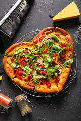 Stand with tasty heart shaped pizza and cheese on black background