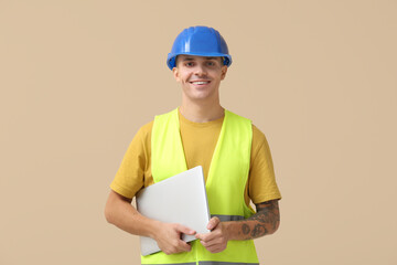 Young male engineer with laptop on beige background