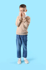 Ill little boy with tissue sneezing on blue background