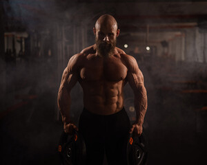 Fototapeta na wymiar Muscular bald shirtless man holding weight plates. A bodybuilder shows off his form in the gym.