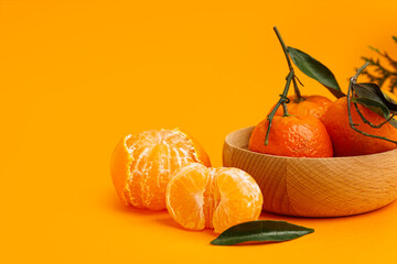 Wooden bowl with tasty tangerines and leaves on orange background
