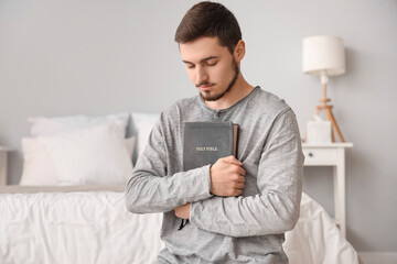 Young man with Bible praying in bedroom