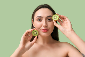 Beautiful young woman with tasty kiwi on green background