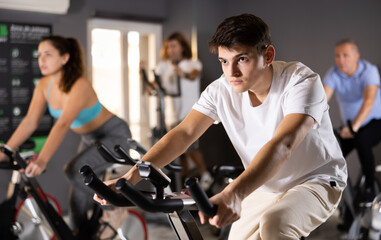 Motivated young guy leading healthy active lifestyle doing cardio workout on exercise bike in gym - obrazy, fototapety, plakaty
