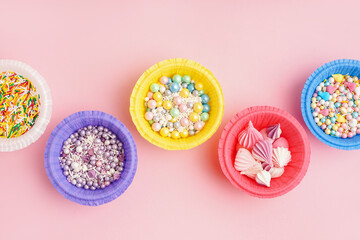 Paper bowls with colorful sweet sprinkles and meringue on pink background