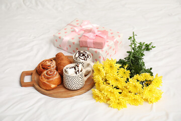 Yellow flowers with gifts, hot chocolate and sweets on bed in room. International Women's Day celebration