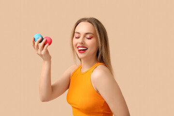 Happy young woman with sweet macaroons on beige background