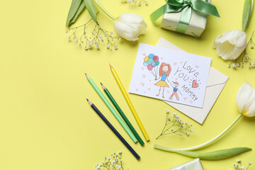 Flowers with kid drawing, pencils and gift box on yellow background. Mother's Day celebration - obrazy, fototapety, plakaty