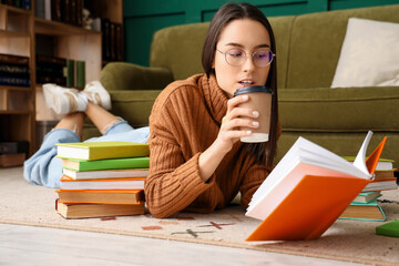 Young woman with book drinking coffee on floor at home
